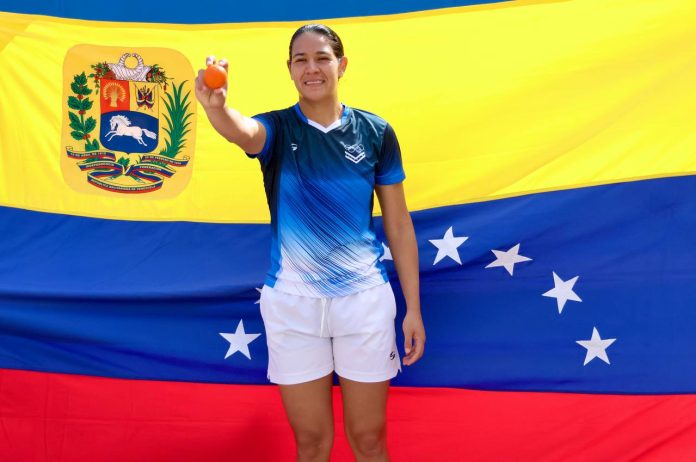 Atleta venezolana sosteniendo una pequeña pelota naranja frente a la bandera de Venezuela