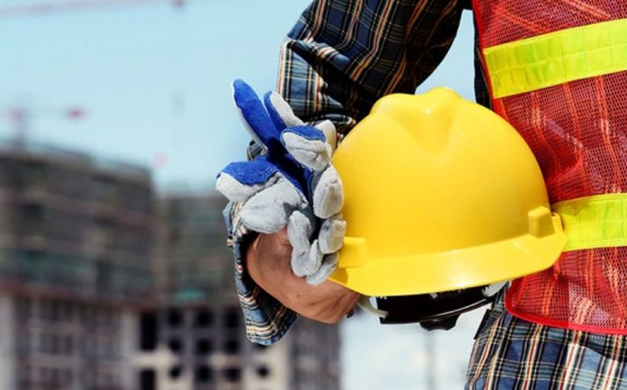 Trabajador de la construcción sosteniendo un casco amarillo y guantes de protección