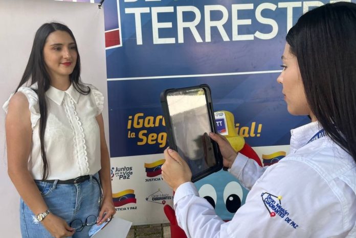 Funcionaria utilizando una tableta digital para fotografiar o registrar a una ciudadana frente a un banner institucional